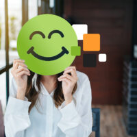 Frau hält sich grünen fröhlichen Smiley vors Gesicht.