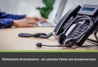 Telefonische Erreichbarkeit - ein zentraler Faktor des Kundenservices. Telefon und Headset im Vordergrund eines Schreibtisches, an dem jemand arbeitet.